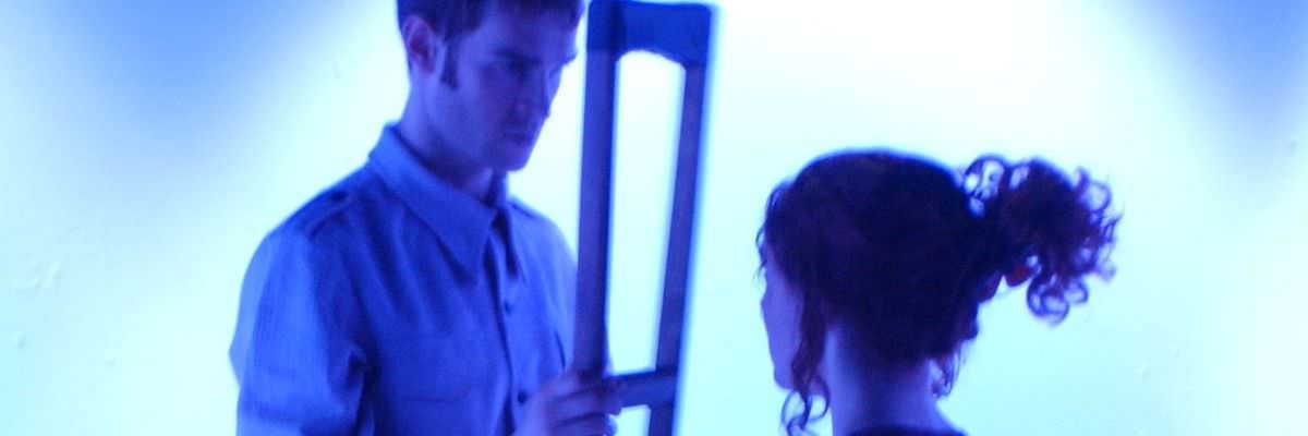 Eyolf is looking at Rita through his crutch. The lighting is a blue wash.