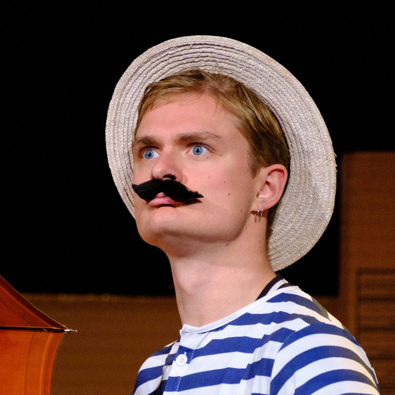 Head shot of a young man with a Victorian moustache wearing a straw and striped swimming costume.