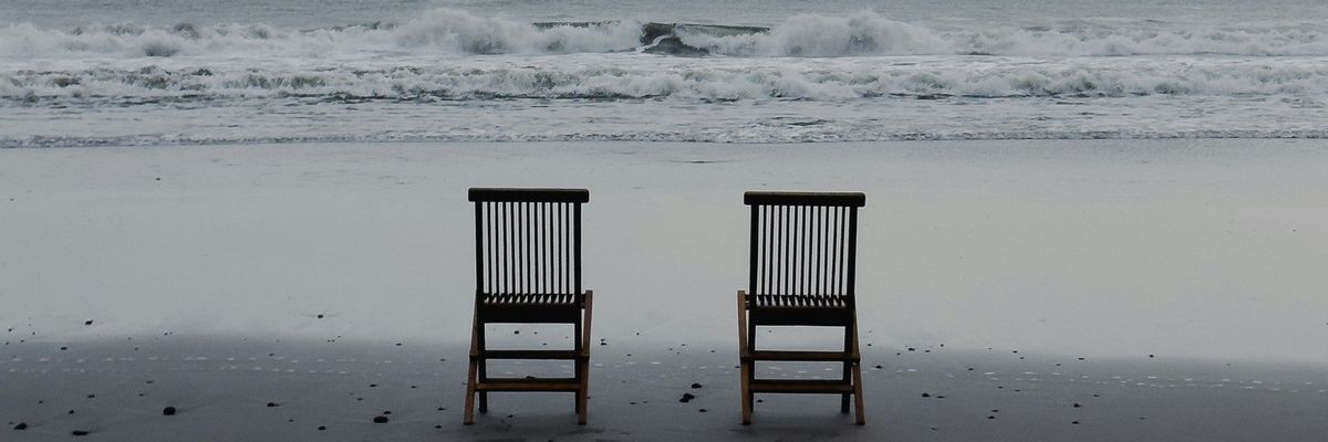 Two empty chairs on a beach, facing the sea