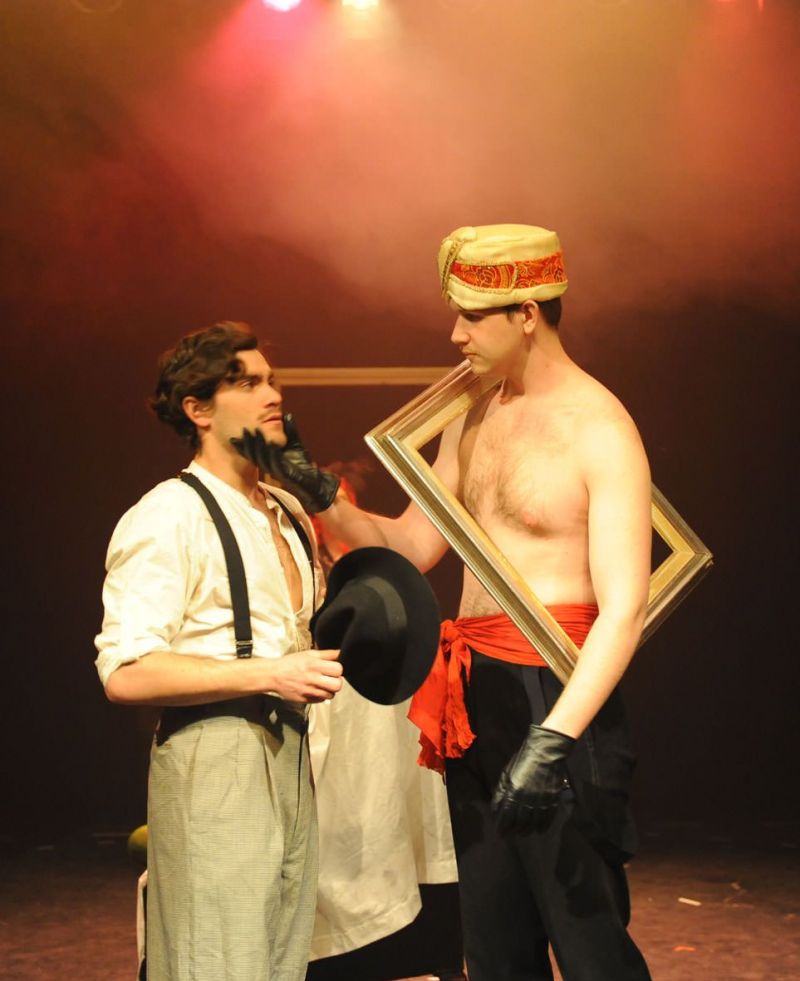 Peer Gynt is being examined by Madam Begriffenfeldt&#039;s tall and imposing assistant, who is bare-chested and wearing black leather gloves, a red waist band and an exotic hat.