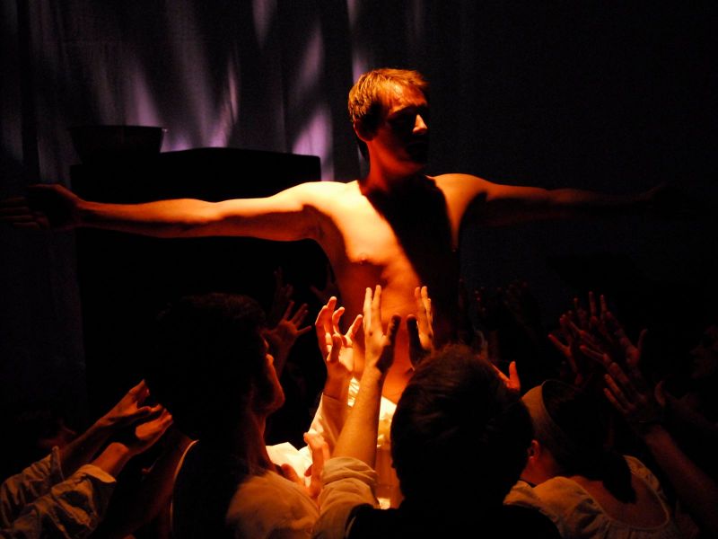 A young bare-chested man is surrounded by a crowd of people. He is holding his arms out resembling the Christ&#039;s crucifixion.
