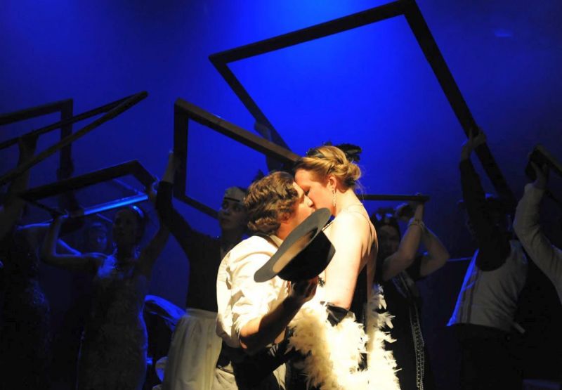 Peer Gynt and Green-Eye are kissing against a backdrop of picture frames in a dark blue light suggesting night.