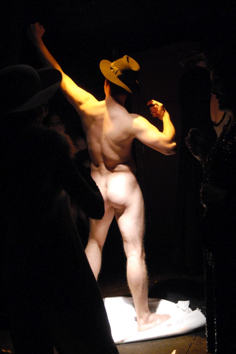 Peer Gynt is posing nude like a Michelangelo&#039;s David, wearing only his trilby, with his back to the audience.